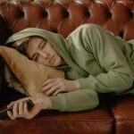 Man in Gray Hoodie Lying on Brown Leather Couch