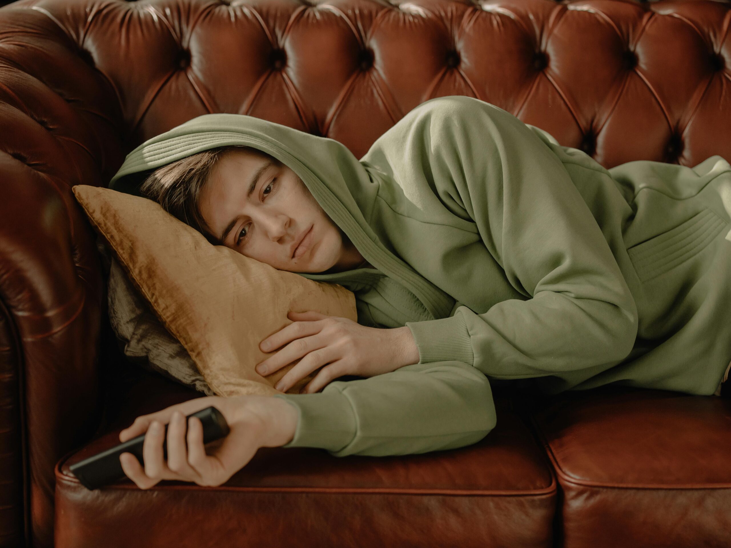 Man in Gray Hoodie Lying on Brown Leather Couch