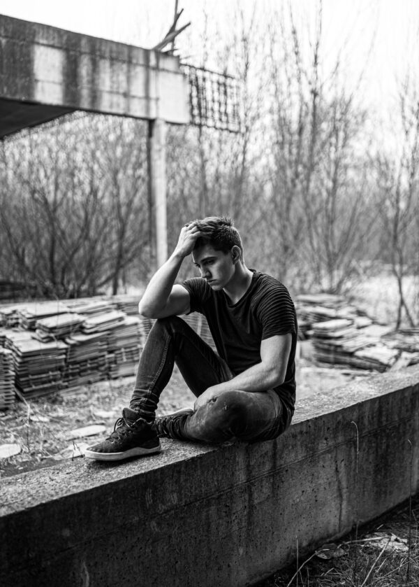 A man sits alone, deep in thought, in a monochrome urban setting.