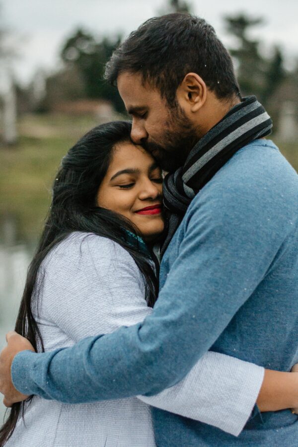 A loving couple embraces outdoors on a cool day, sharing a tender moment.