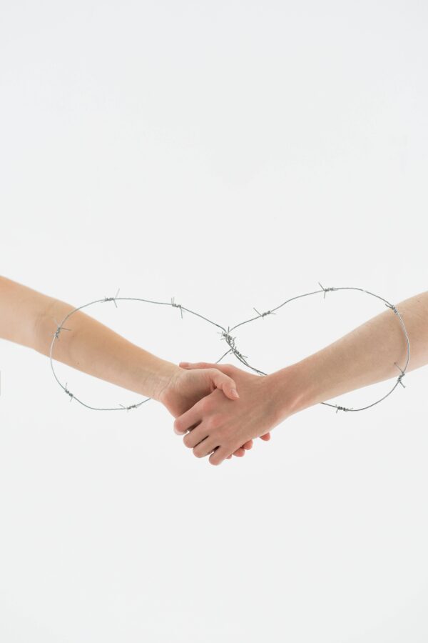 Two hands clasped within a circular barbed wire loop, symbolizing complex relationships.
