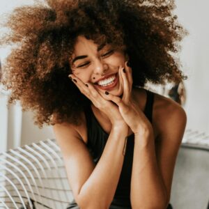 A cheerful woman with an afro hairstyle sitting indoors, showcasing happiness and style.