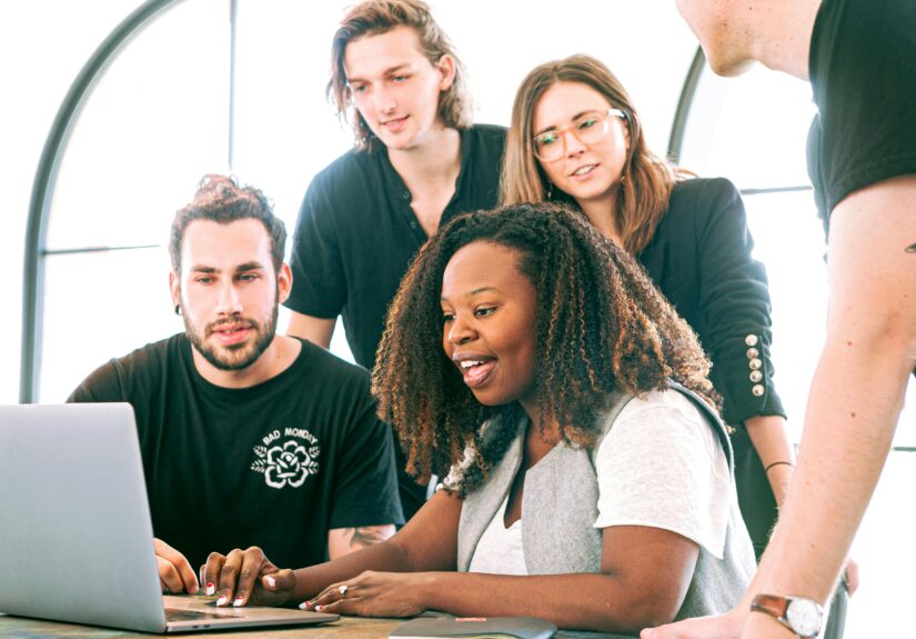 A diverse group of young professionals collaborating around a laptop in a modern office setting. Perfect for business or tech concepts.