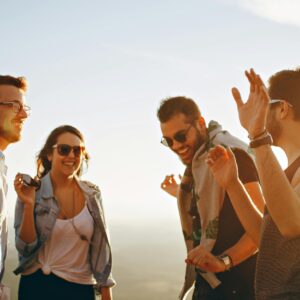 A group of friends laughing and dancing outdoors on a bright sunny day, showcasing friendship and joy.