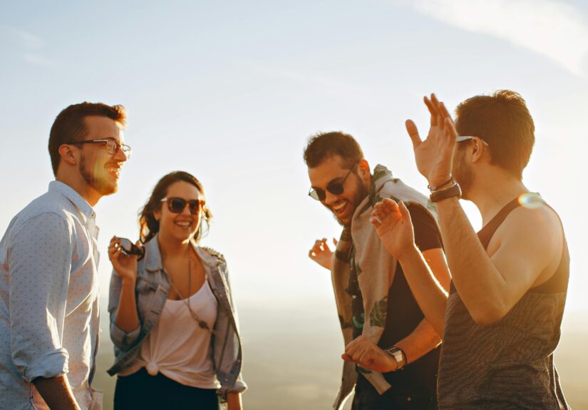 A group of friends laughing and dancing outdoors on a bright sunny day, showcasing friendship and joy.