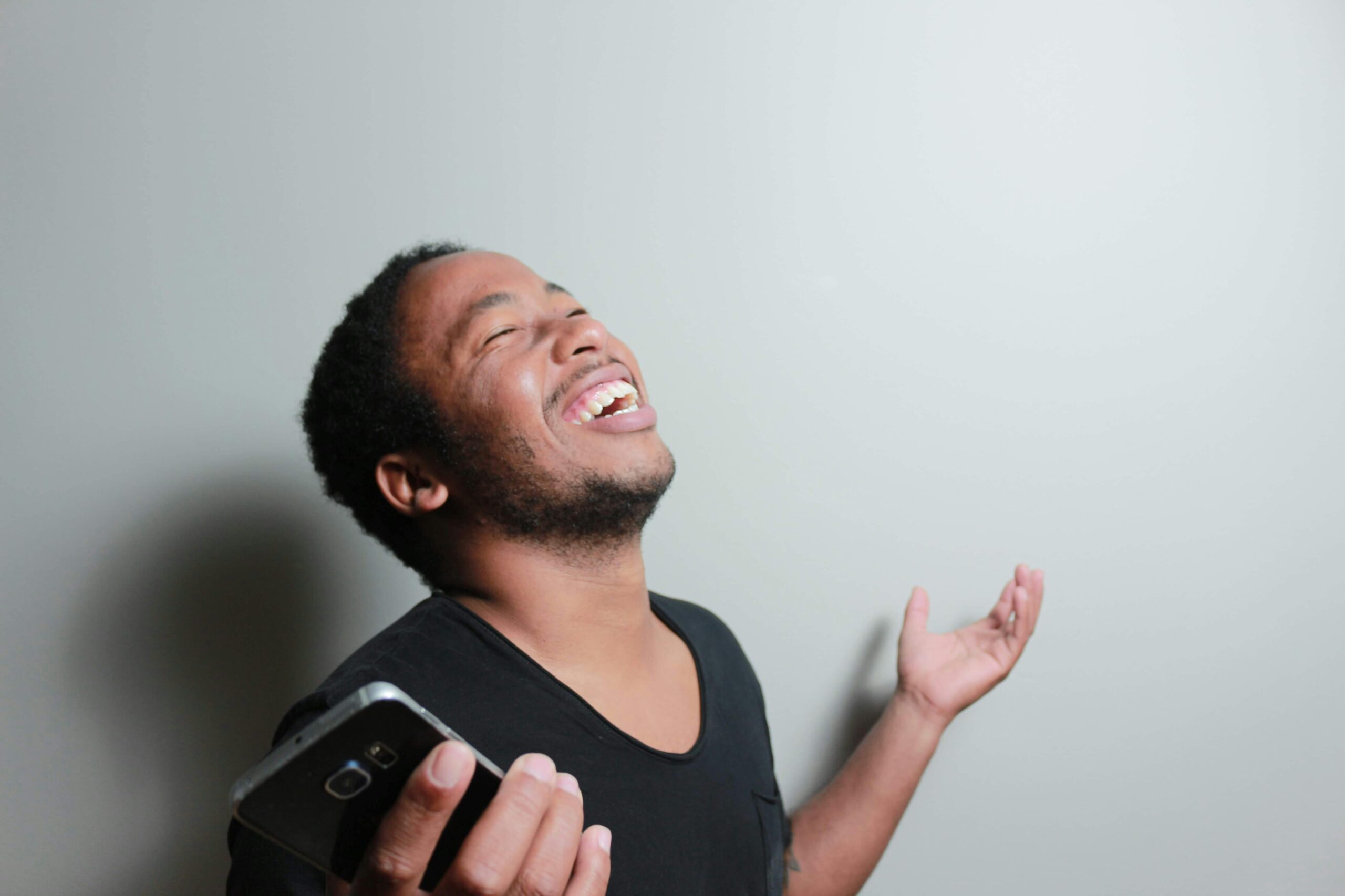 A cheerful man joyfully expresses happiness while holding a smartphone indoors.
