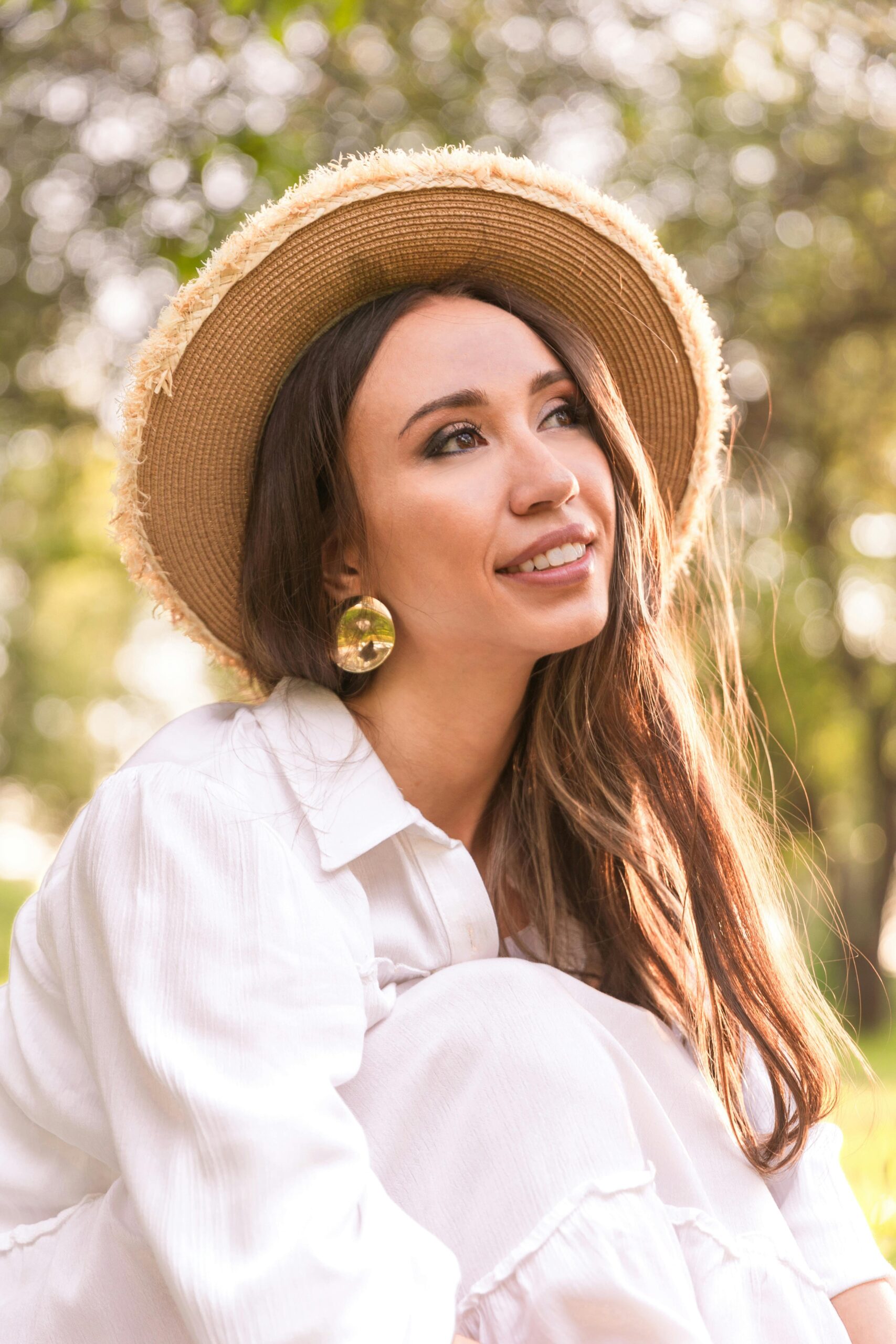 Young woman in a straw hat smiling outdoors, surrounded by nature.