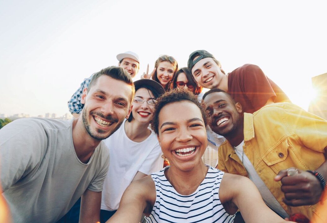 A diverse group of friends taking a joyful selfie outdoors during sunset.