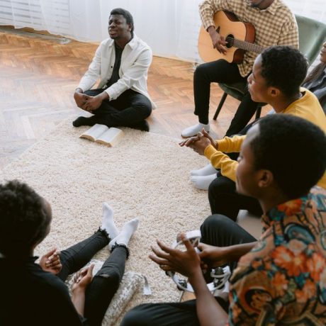 A diverse group of people gathered indoors for prayer and music, featuring a guitarist leading worship.