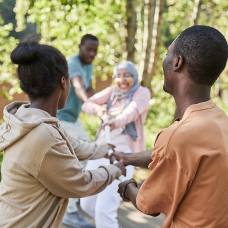 A cheerful group of diverse friends playing tug of war in a sunny park setting.